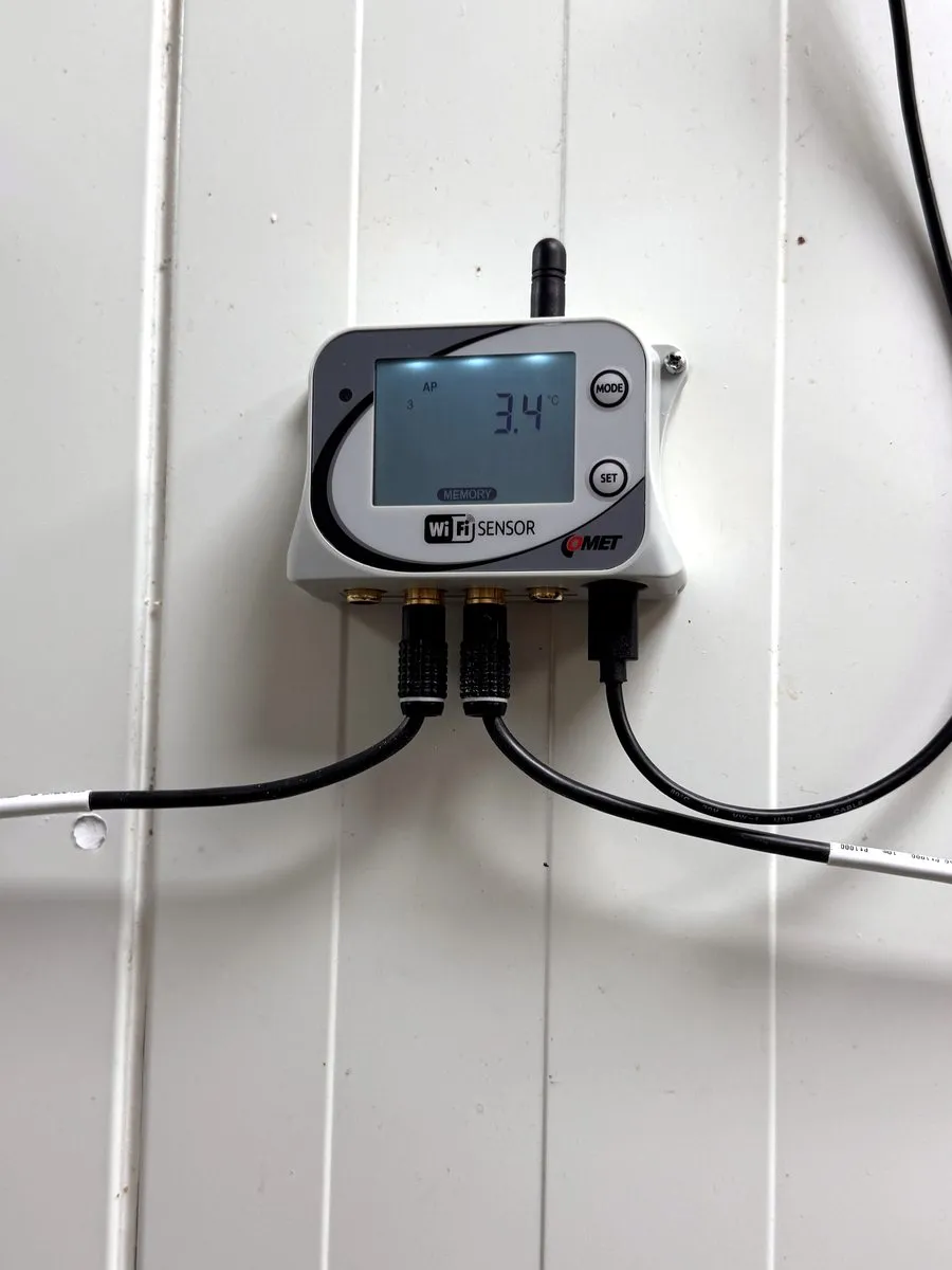 Wi-Fi datalogger Comet se dvěma sondami na stěně chladírny, displej ukazuje 3,4 °C